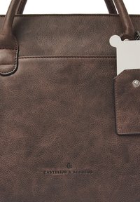 Bruine leren tas met een gestructureerde oppervlakte, voorzien van dubbele handvatten en een label. De merknaam is onderaan gecast. Klassiek ontwerp.