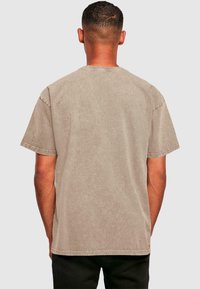T-Shirt mit kurzen Ärmeln in Taupe, leicht verblasster Struktur, Rundhalsausschnitt und sichtbaren Nähdetails an den Kanten. Rückansicht gezeigt.