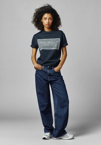 Marineblauwe katoen t-shirt met een grijze "RED BULL RACING" logo, gecombineerd met wijdvallende blauwe jeans en lichtgrijze sportschoenen.