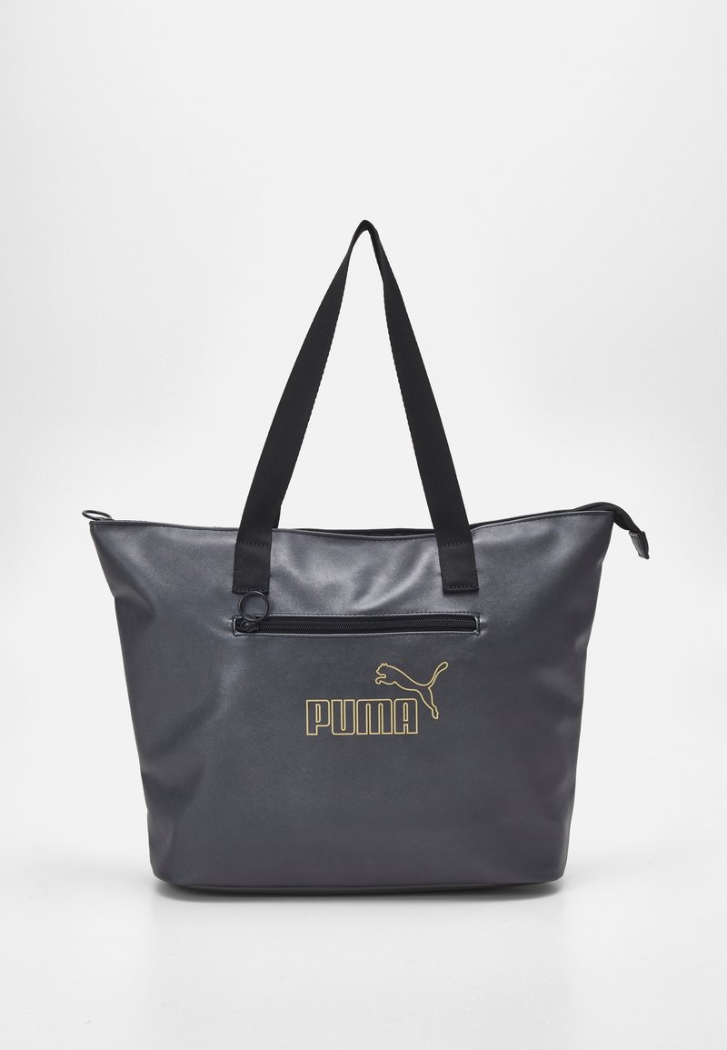 Bolso tote negro de Puma con logo dorado, bolsillo frontal con cremallera y largas correas negras para el hombro sobre un fondo blanco.
