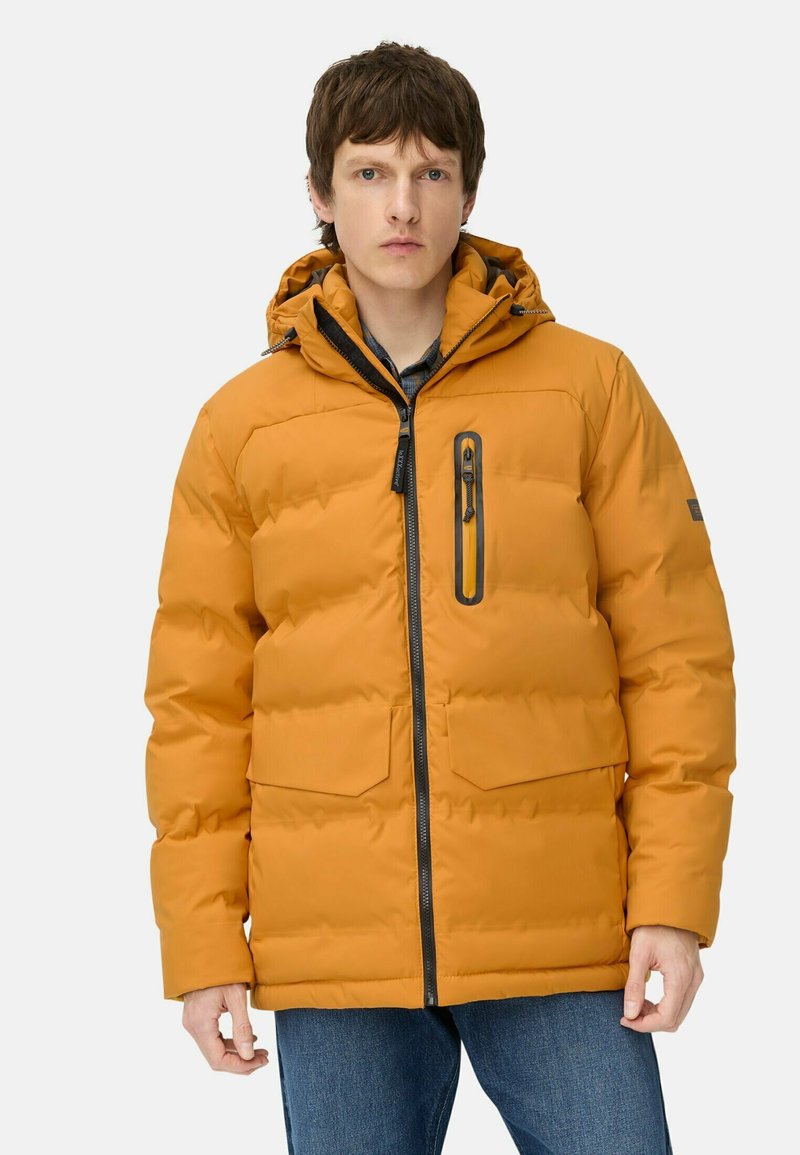 Oranje gewatteerde jas met een rits aan de voorkant, capuchon en twee voorzakken. Met een zwarte rits en een zakje op de linkerkant van de borst voor extra detail.