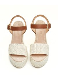 Sandalias de plataforma beige con tiras frontales entrelazadas y correas de tobillo de cuero marrón con cierres de hebilla dorada, vistas desde arriba.