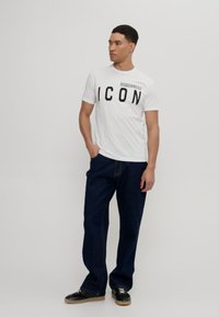White short-sleeve T-shirt with large black "ICON" text and "DSQUARED2" logo. Paired with dark blue loose-fit pants and black sneakers.