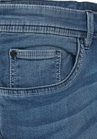 Denim-Jeans in mittlerem Blau mit einer einzelnen Gesäßtasche, ausgestattet mit einem schwarzen Knopf und weißen Nähten. Weicher, strukturierter Stoff mit einem ausgebleichten Finish.
