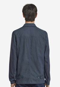 Marinblå knapplång jacka med rak skärning, långa ärmar och två stora knappar i fållen, med en slät textur och minimala sömmar.