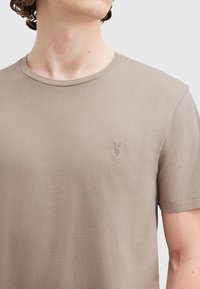 T-shirt a maniche corte, con collo rotondo, in una leggera miscela di cotone beige. Presenta un logo ricamato discreto sulla parte sinistra del petto.