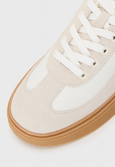 Baskets en suède beige avec des accents en cuir blanc, bout rond, lacets blancs et semelle en gomme texturée. Comprend des œillets en or pour les lacets.