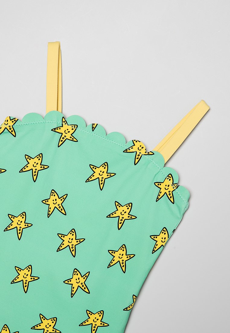 Jednoczęściowy strój kąpielowy w miętowym kolorze z falbankowym dekoltem, ozdobiony wzorem żółtych gwiazd obrysowanych na czarno oraz żółtymi ramiączkami.