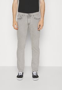 Jeans en denim gris clair avec une coupe slim, design à cinq poches et coutures contrastées. Associés à des baskets noires et un t-shirt noir ajusté.