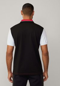 Schwarz-weißes Poloshirt mit kurzen Ärmeln; schwarzer Körper, weiße Schultern, roter Kragenakzent und rote Steppnähte am Saum.