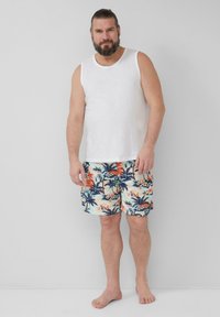 Weiße ärmellose Bluse und hell gemusterte Badeshorts mit blauen Palmen, orangen Blumen und einem hellen Hintergrund. Barfuß.