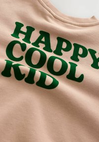 Beiger Stoff mit grünem Samttext, der "GLÜCKLICHER COOLER KID" in fetten, abgerundeten Buchstaben liest.