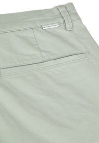 Un tissu vert clair avec une texture lisse présente une poche arrière et une étiquette avec la marque "TOM TAILOR" cousue sur la ceinture.