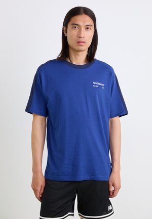 T-shirt en coton bleu à manches courtes et col rond. Présente des accents d'épaules bleu marine et un logo "New Balance" blanc sur la poitrine.