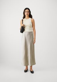 Top sans manches crème, jupe maxi en satin gris clair, sac à main noir et chaussures plates. Textures douces et éléments de design simples.