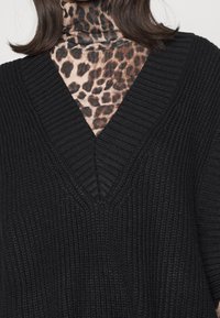 Svart stickad tröja med djup V-ringning och ribbad struktur. Underst en polotröja med leopardmönster i brunt och beige.