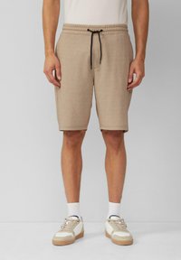 Beige Strickshorts mit elastischem Bund und schwarzem Kordelzug. Glatte Textur, knielang, kombiniert mit hellen Sneakers und weißen Socken.