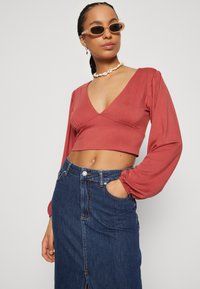 Rust crop top s dugim napuhanim rukavima, V-izrez; uparen s traper suknjom visokog struka koja ima prednji rez i džepove.