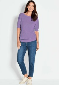 Lila Kurzarmpullover mit rundem Halsausschnitt, kombiniert mit hellblauen Jeans und beigen Sneakern. Der Pullover hat eine weiche Textur.