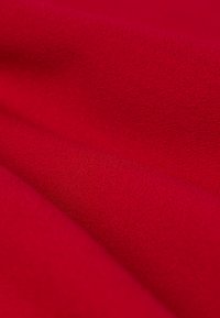 Tissu rouge avec une surface texturée et douce, présentant une légère brillance. Le matériau semble épais et se plie en douceur, mettant en valeur la profondeur de sa couleur.