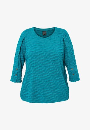 Turkizna majica iz teksturirane tkanine, s valovitim uzorcima, rukavima do tri četvrtine i gumbima kao ukrasom na rukavima. Okrugli izrez.