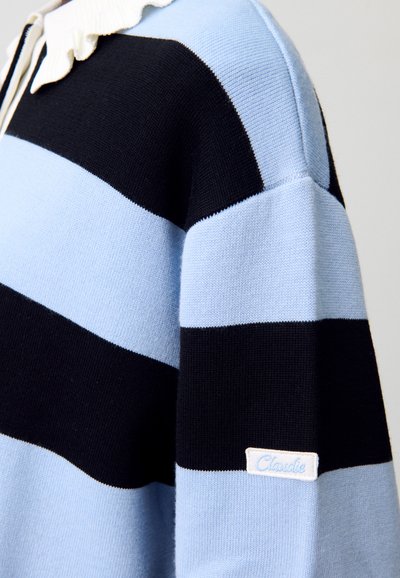 Suéter de algodón tejido con rayas horizontales en azul claro y negro, con un cuello en forma de concha blanco y una pequeña etiqueta en el dobladillo.