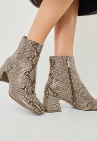 Metallic brown ankle boots with a textured, snake-skin pattern. Features a side zipper and a block heel for stability. Smooth finish.
