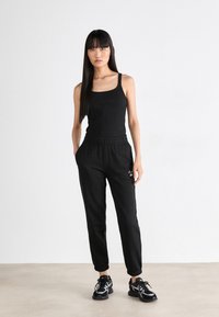Juodas tanktopas su tekstūru, derinamas su juodomis sportinėmis kelnėmis, turinčiomis elastingą juosmenį ir užapvalintais kulkšniais. Juodi sportiniai bateliai.
