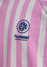 Grått tyg med vertikala rosa och vita ränder. Har en blå cirkulär logotyp och texten "hummel SPORTSWEAR" under logotypen.