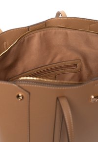 Intérieur de sac à main en cuir fauve avec doublure en tissu lisse, comprenant une poche zippée et un compartiment principal spacieux.