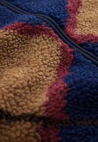 Colorful fleece fabric featuring a brown, maroon, and blue abstract pattern, with a soft, textured surface and a seamless design.
