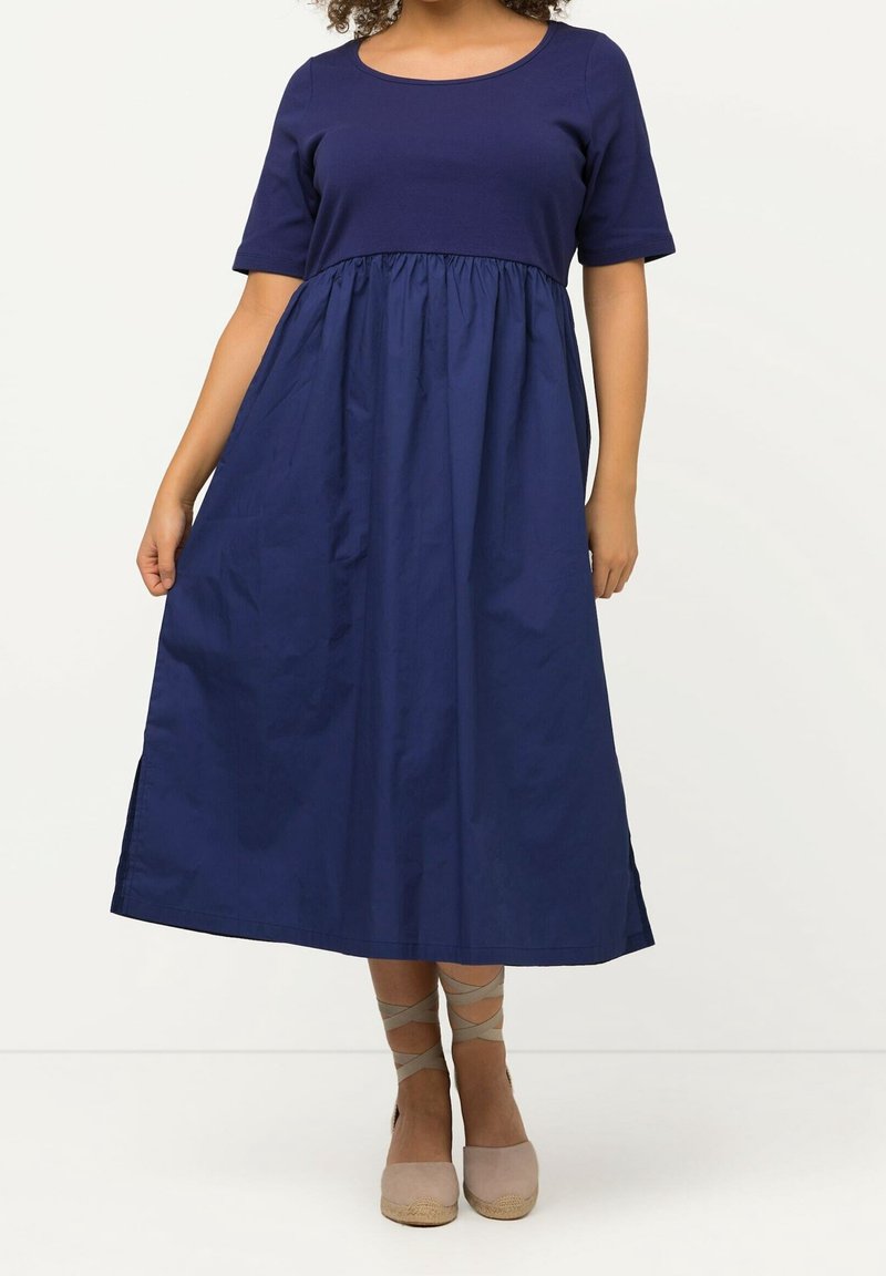 Marinblå bomullsklänning med rund halsringning, korta ärmar och insydd midja, som når till mitten av vaden. Slät textur, minimalistisk design.