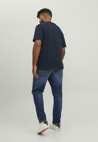 Navyblaues Baumwoll-T-Shirt kombiniert mit dunklen Jeans. Das Outfit umfasst weiße Sneaker mit schwarzen Akzenten und minimalen Nähten.