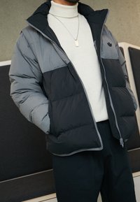 Grå och svart puffjacka med dragkedja fram, med hög krage och horisontell söm. Bärs över en polotröja.