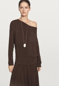 Brązowa, długosleeve'owa bluzka na ramiączkach z marszczonym dołem. Miękka tkanina i srebrny owalny naszyjnik jako akcent.