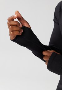 Fekete, testhez simuló, hosszú ujjú ruhadarab, hüvelykujjlyukakkal, rugalmas anyagból készült. Simább textúrával és varrás nélküli cuffokkal rendelkezik.
