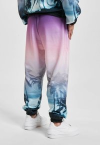 Pantaloni jogger con gradiente sfumato che passa dal viola al blu, con un motivo di palme nella parte inferiore, dotati di polsini e vita elastica.