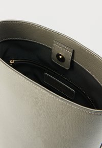 Geantă tote din piele gri cu finisaj texturat, având interior negru, buzunar cu fermoar și etichetă de marcă pe lateral.