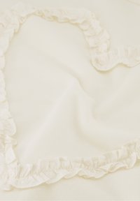 Witte stof met een zachte textuur, voorzien van een gerimpelde rand langs de rand, wat een zachte, vloeiende uitstraling creëert.