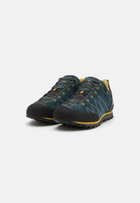 Chaussures de randonnée bleu et noir avec une tige en suede texturé, accents jaunes, capuchon en caoutchouc à l'avant, et lacets à motif. Conception de semelle à crampons agressifs.