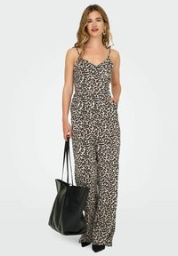 Tutina con stampa leopardata, spalline sottili e vita aderente; gambe larghe, tasche; abbinata a una grande borsa nera e tacchi a punta neri.