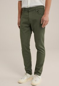 Gröna bomullshängselbyxor med slim fit, med dragkedja, fram- och bakfickor, och i kombination med vita sneakers.