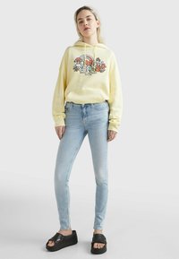 Sudadera amarilla con diseño gráfico, combinada con jeans skinny de color azul claro y sandalias de plataforma negras. Texturas suaves; corte relajado.
