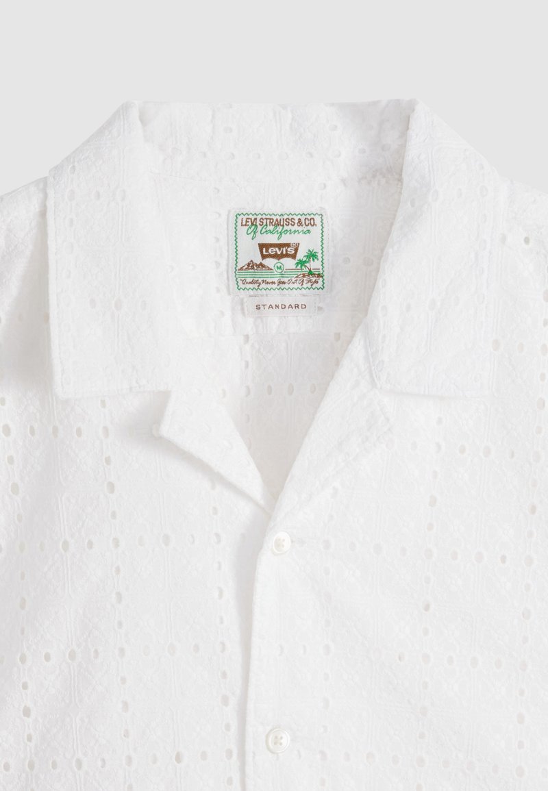 Weißes Hemd mit Ösenmuster, Camp-Kragen, zwei sichtbaren Knöpfen und Etikett von Levi's Strauss & Co. mit der Aufschrift "Standard" im Innenkragen.
