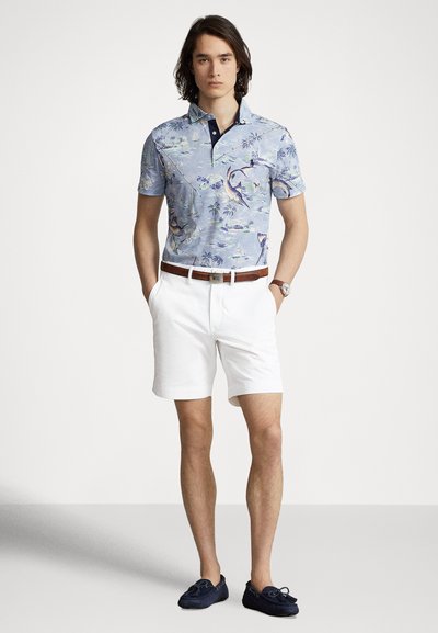 Svetlomodré polo tričko s kvetinovým vzorom, námornícky modrý golier; biele šortky a námornícky modré mokasíny. Viditeľný detail hnedej opasky a náramkových hodiniek.