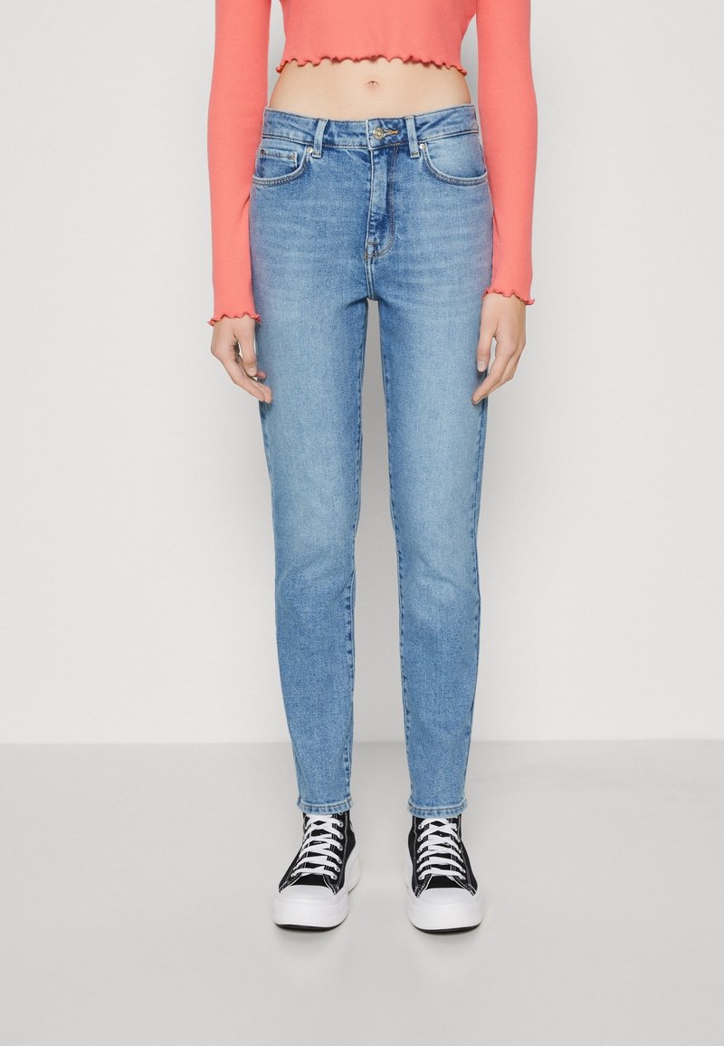 Ljusblå jeans med smal passform, hög midja, fem fickor och knappgylf. Matchat med svarta och vita sneakers.