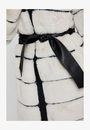 Abrigo de piel sintética blanca con rayas negras, que presenta un cinturón de cuero negro y cierre frontal con cremallera. Textura suave y secciones acolchadas.