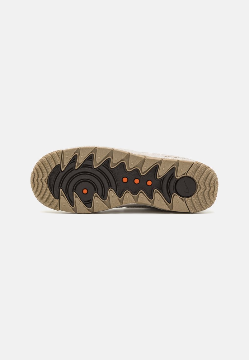 Semelle de sneaker beige et noire avec des bords en zigzag et quatre petites accentuations circulaires orange au centre sur un fond blanc.