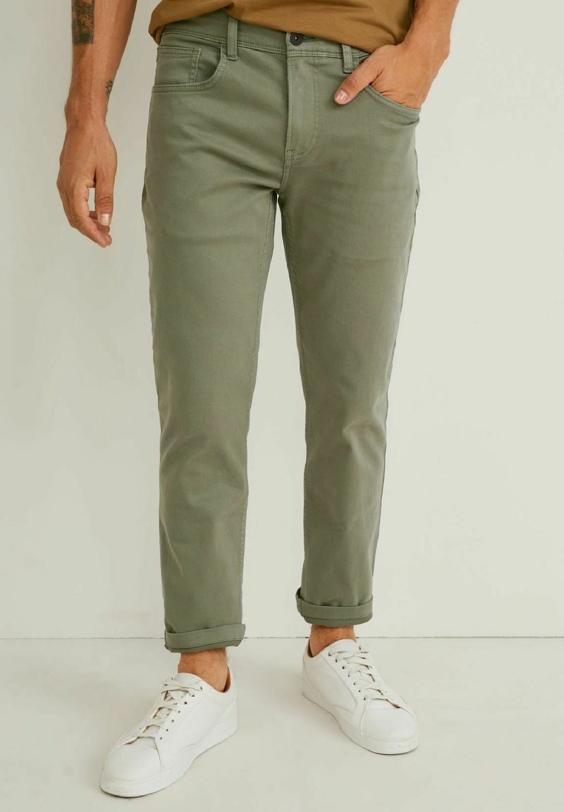 Olivgrön bomullschinos med slim fit, med uppvikta mudd och sidofickor. Kombineras med vita sneakers för en avslappnad stil.