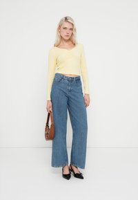 Żółty krótki top z długim rękawem i dekoltem w serek, zestawiony z wysokim stanem i szerokimi nogawkami niebieskich dżinsów. Czarne, spiczaste baleriny i brązowa torba na ramię.